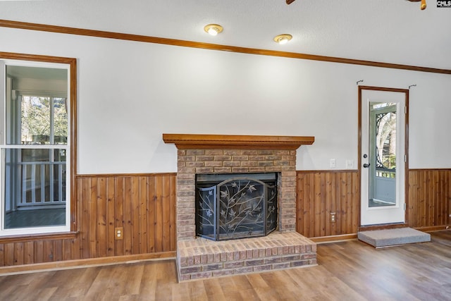 unfurnished living room with wooden walls, wainscoting, wood finished floors, a textured ceiling, and a fireplace