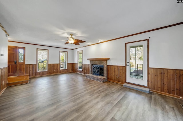 unfurnished living room with ceiling fan, a fireplace, wood finished floors, and wainscoting