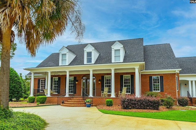 new england style home featuring covered porch, brick siding, and roof with shingles