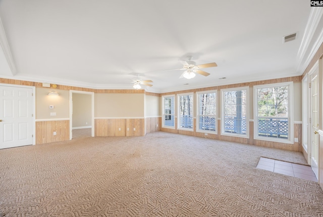 carpeted empty room featuring wood walls, visible vents, ornamental molding, and wainscoting