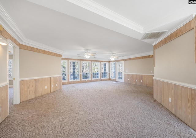 empty room with crown molding, visible vents, light colored carpet, wainscoting, and wood walls