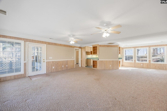 unfurnished living room featuring light carpet, wood walls, visible vents, and ornamental molding