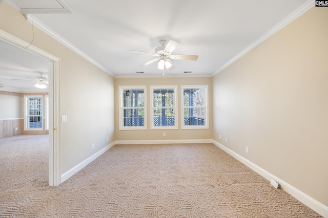 carpeted empty room with ceiling fan, visible vents, baseboards, attic access, and crown molding