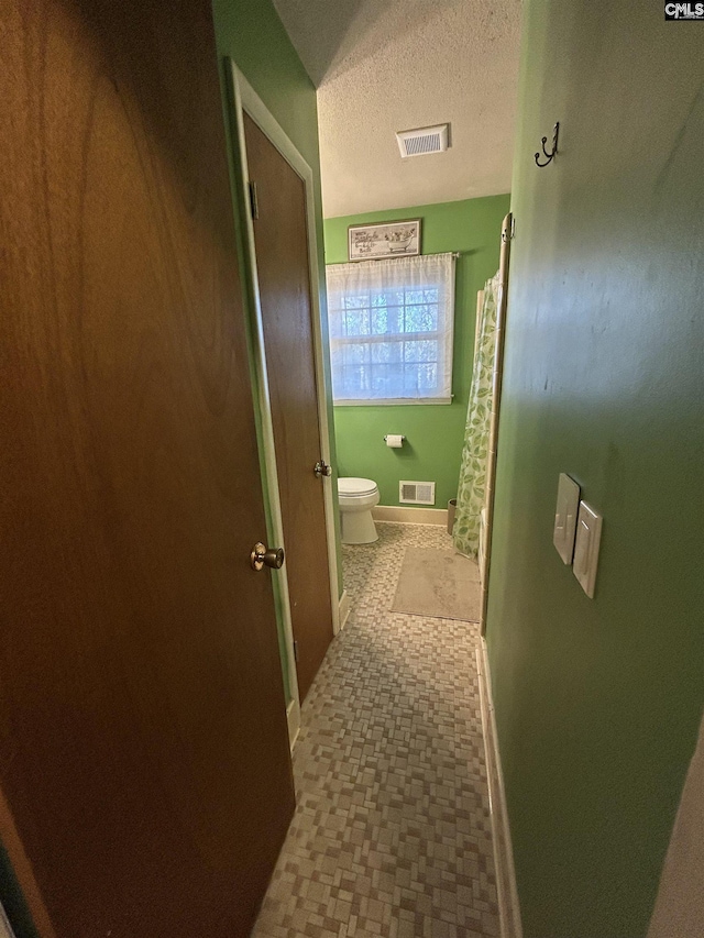 hallway with baseboards, visible vents, and a textured ceiling