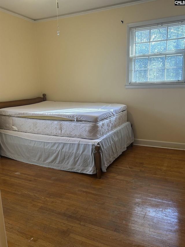 unfurnished bedroom featuring baseboards, hardwood / wood-style floors, and crown molding