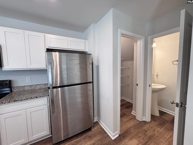 kitchen featuring dark wood-style floors, white cabinets, dark stone countertops, and freestanding refrigerator