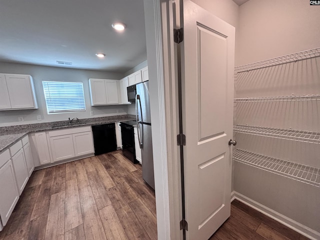 kitchen featuring white cabinets, dark stone countertops, dark wood-style flooring, black appliances, and a sink