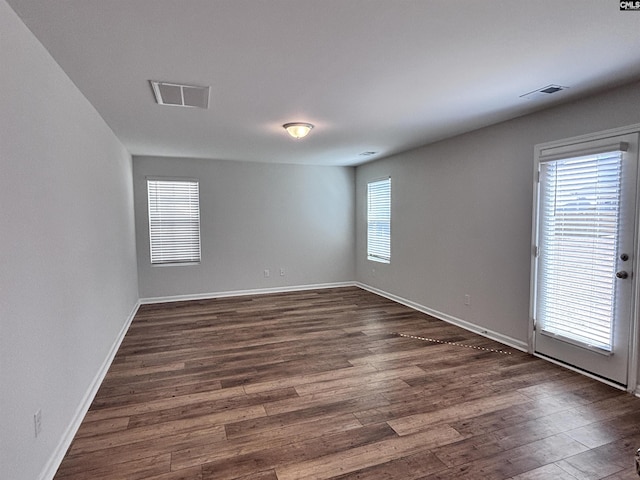 spare room featuring dark wood-style flooring, visible vents, and baseboards