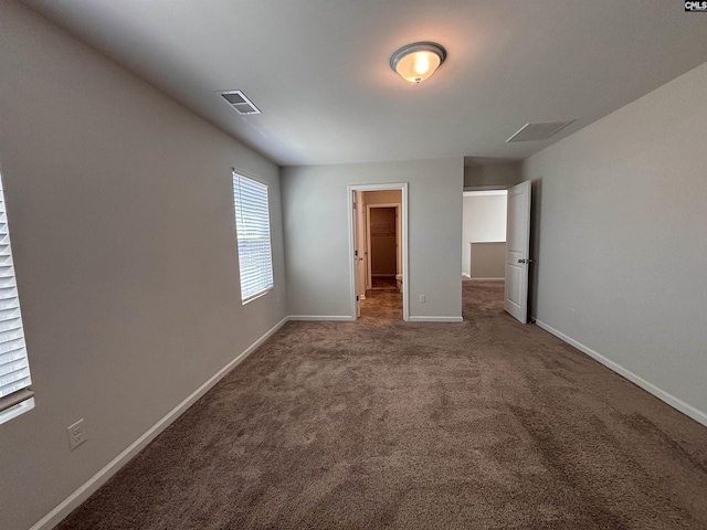 unfurnished bedroom with a walk in closet, carpet flooring, visible vents, and baseboards