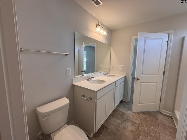 bathroom featuring toilet, double vanity, visible vents, and a sink