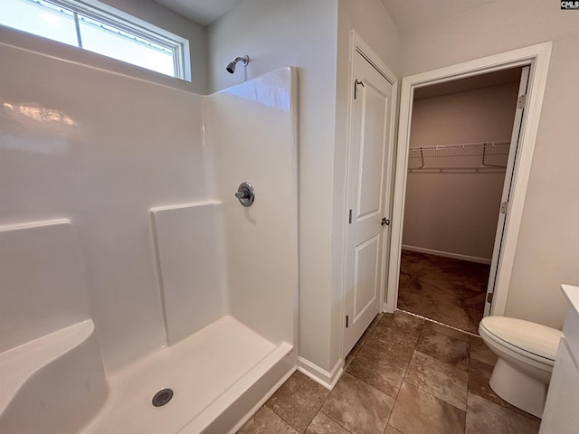 full bathroom with a walk in closet, a shower stall, toilet, and baseboards