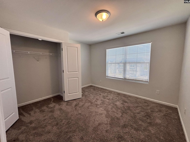 unfurnished bedroom with dark colored carpet, a closet, visible vents, and baseboards