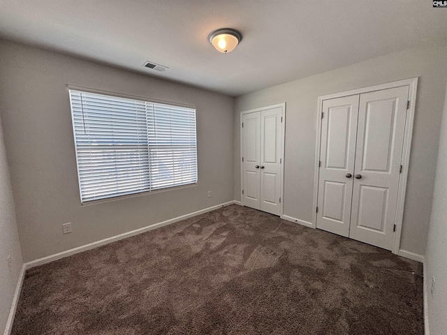 unfurnished bedroom with multiple closets, visible vents, dark carpet, and baseboards