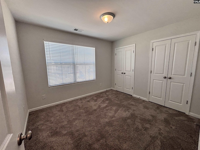 unfurnished bedroom featuring baseboards, visible vents, dark carpet, and two closets