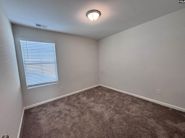 empty room with dark colored carpet, visible vents, and baseboards