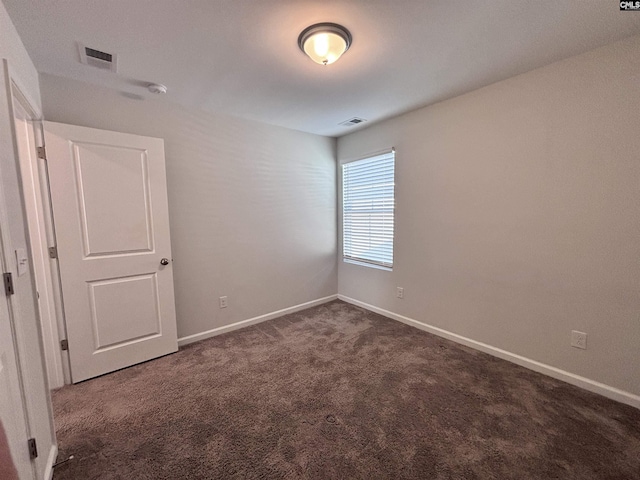 empty room with visible vents, dark carpet, and baseboards