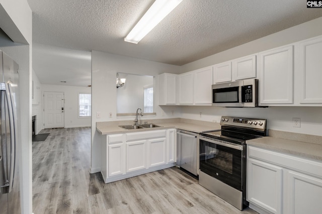 kitchen featuring appliances with stainless steel finishes, a sink, light wood-style flooring, and white cabinets