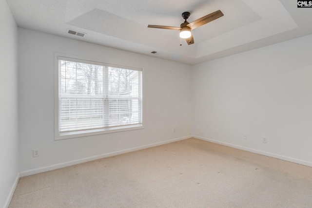 empty room featuring a raised ceiling, light carpet, and baseboards