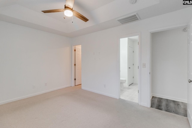 unfurnished bedroom with carpet, a tray ceiling, visible vents, connected bathroom, and baseboards