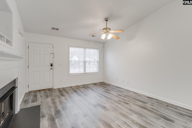 unfurnished living room with baseboards, visible vents, a ceiling fan, wood finished floors, and a fireplace