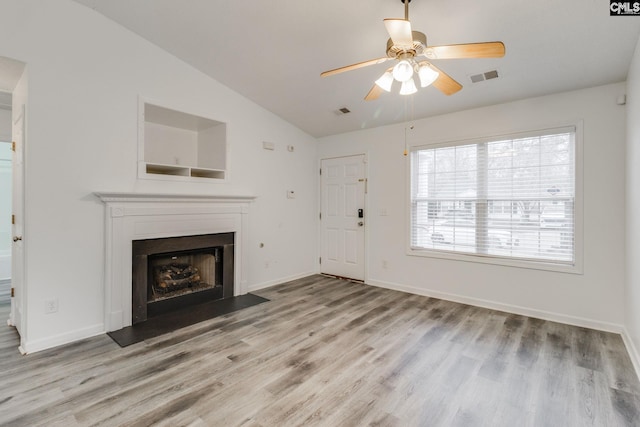 unfurnished living room with baseboards, visible vents, lofted ceiling, a fireplace with flush hearth, and wood finished floors