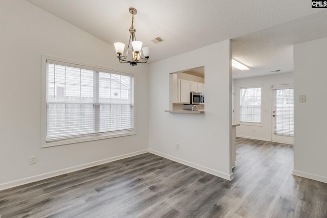 unfurnished dining area featuring a notable chandelier, dark wood-type flooring, visible vents, and baseboards