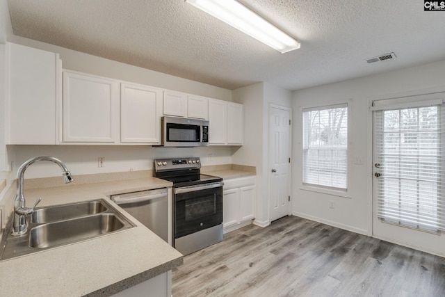 kitchen with visible vents, appliances with stainless steel finishes, white cabinets, a sink, and light wood-type flooring