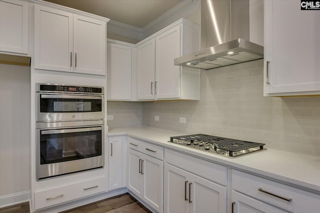 kitchen with tasteful backsplash, white cabinets, dark wood finished floors, stainless steel appliances, and wall chimney range hood