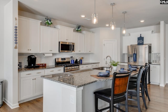 kitchen featuring white cabinets, appliances with stainless steel finishes, light wood-style floors, a kitchen bar, and a sink