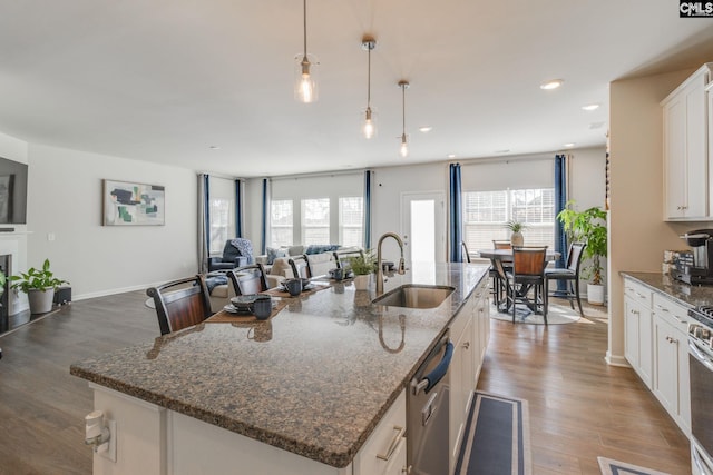 kitchen featuring wood finished floors, appliances with stainless steel finishes, a sink, and a center island with sink