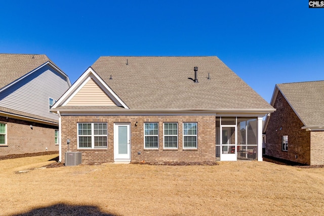 back of property featuring central AC unit, a sunroom, roof with shingles, a yard, and brick siding