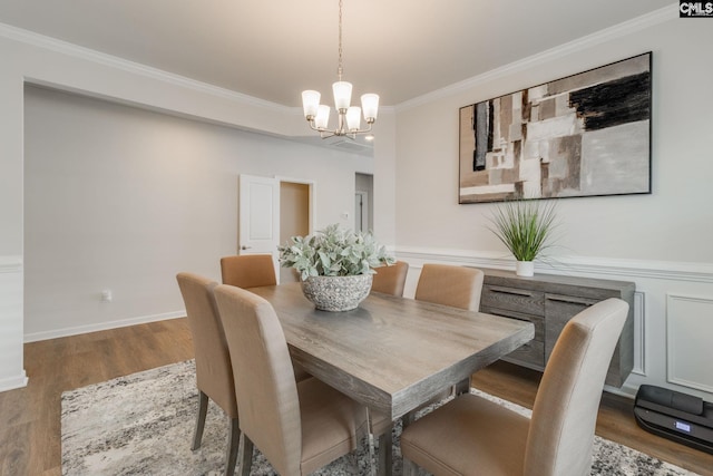 dining area featuring a notable chandelier, wood finished floors, baseboards, wainscoting, and crown molding