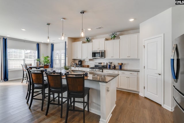 kitchen featuring a breakfast bar area, a sink, visible vents, appliances with stainless steel finishes, and decorative backsplash