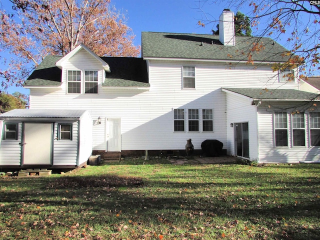 rear view of property featuring entry steps, a shingled roof, a lawn, a chimney, and an outdoor structure