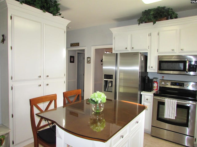 kitchen with light wood-style flooring, white cabinetry, appliances with stainless steel finishes, a center island, and dark countertops