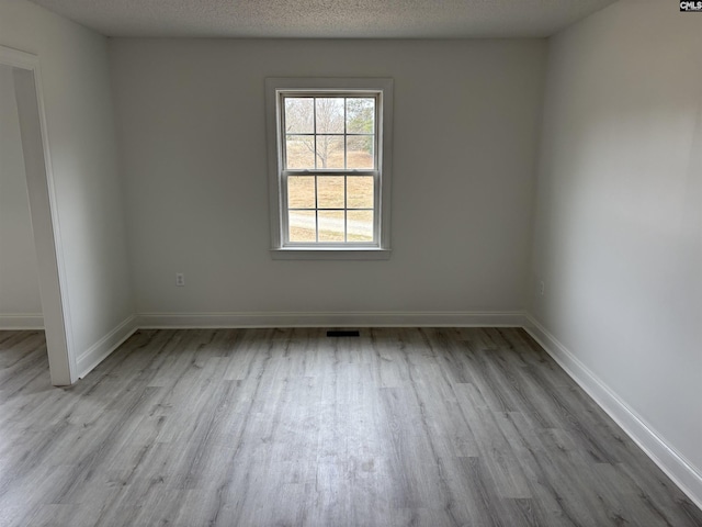 empty room with a textured ceiling, baseboards, and wood finished floors