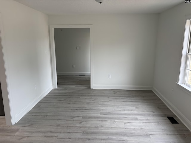 spare room with wood finished floors, visible vents, and baseboards