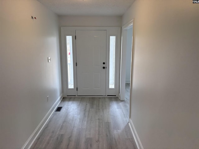 foyer featuring baseboards, wood finished floors, visible vents, and a healthy amount of sunlight