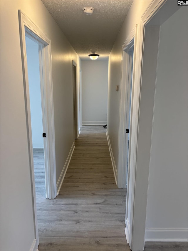 hall with a textured ceiling, wood finished floors, and baseboards