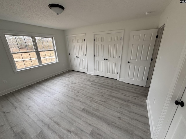 unfurnished bedroom with a textured ceiling, wood finished floors, two closets, and baseboards