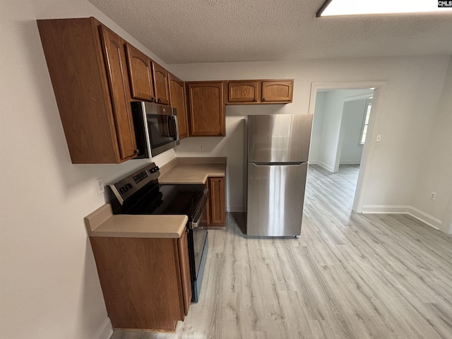 kitchen with a textured ceiling, stainless steel appliances, baseboards, light wood-style floors, and light countertops