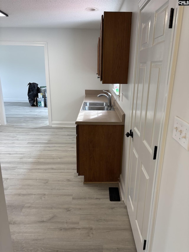 interior space featuring baseboards, light countertops, a textured ceiling, light wood-type flooring, and a sink