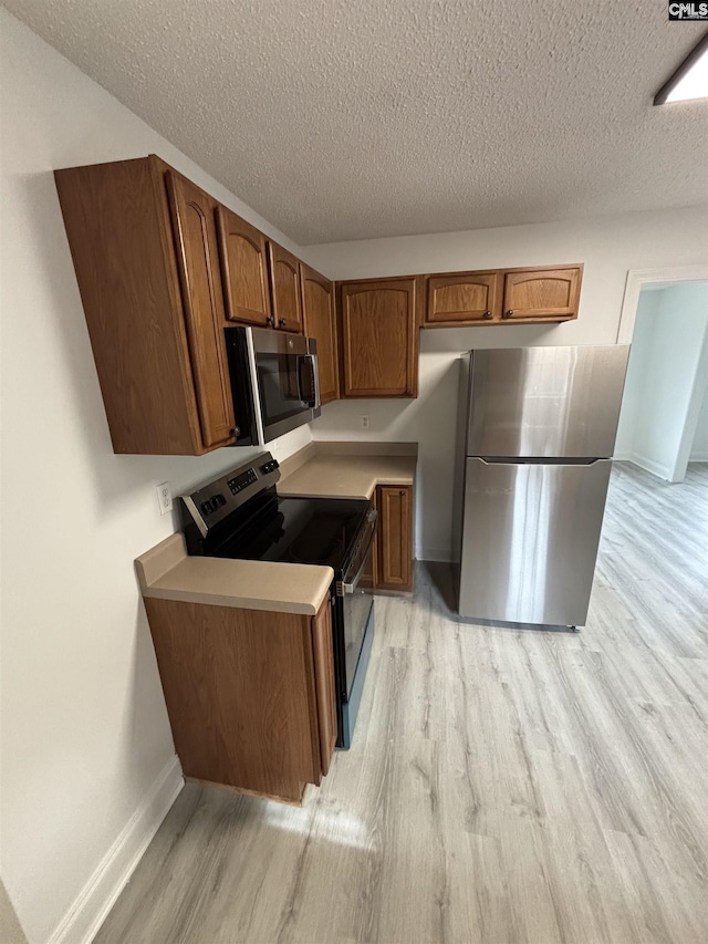 kitchen featuring stainless steel appliances, baseboards, light countertops, light wood finished floors, and brown cabinetry