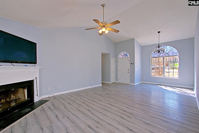 unfurnished living room featuring ceiling fan with notable chandelier, a fireplace, baseboards, and wood finished floors