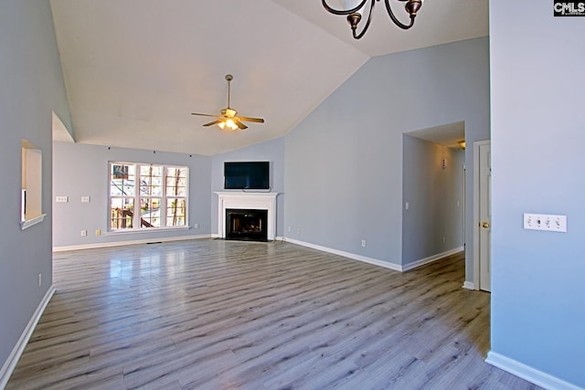 unfurnished living room featuring a fireplace with flush hearth, wood finished floors, high vaulted ceiling, baseboards, and ceiling fan with notable chandelier