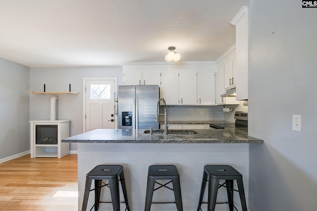 kitchen with under cabinet range hood, a peninsula, a sink, appliances with stainless steel finishes, and backsplash