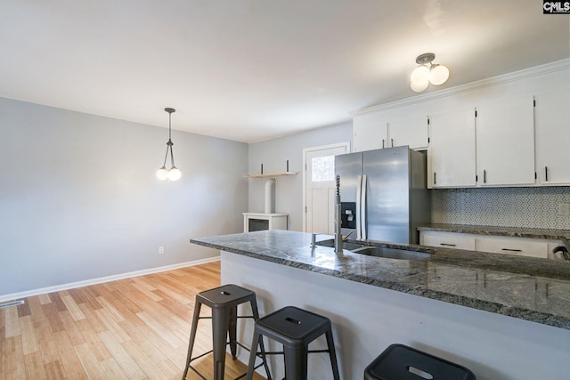 kitchen with stainless steel refrigerator with ice dispenser, light wood-style flooring, decorative backsplash, white cabinets, and a kitchen breakfast bar