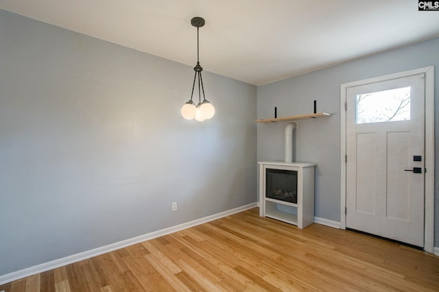 foyer entrance featuring a wood stove, baseboards, and light wood finished floors