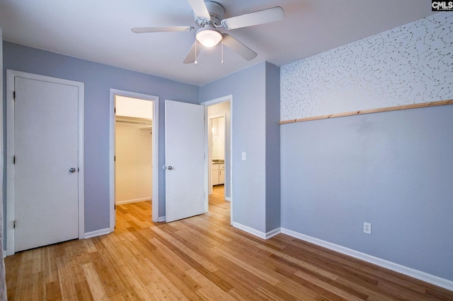 unfurnished bedroom featuring baseboards, ceiling fan, a walk in closet, light wood-type flooring, and a closet