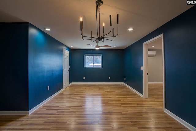 unfurnished dining area featuring ceiling fan with notable chandelier, a wall mounted air conditioner, wood finished floors, and baseboards